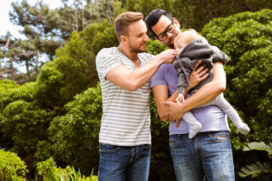 Smiling gay couple with child in garden